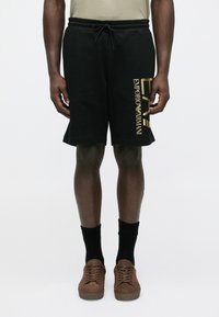 Fekete pamut rövidnadrág gumis derékrésszel és húzózsinórral. Arany "Emporio Armani" logó található a bal oldalon. Laza, hétköznapi kialakítás.
