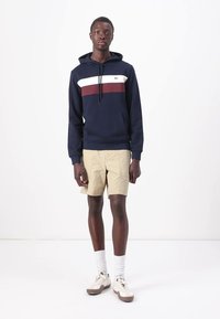 Felpa navy con strisce orizzontali bianche e bordeaux, materiale in cotone, tasca frontale, abbinata a pantaloni cargo khaki e calzini bianchi. Calzature casual.