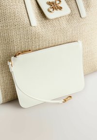 Un grand sac à main tissé beige avec une pochette blanche lisse amovible. La pochette est dotée d'une fermeture éclair dorée et d'une sangle assortie.