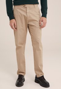 Beige chinos gemaakt van katoen met een rechte pijp design, voorzien van een enkele knoopsluiting en ceintuurlussen, gecombineerd met zwarte leren schoenen.