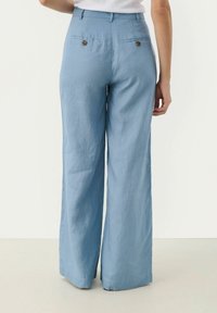 Lichtblauwe wijde broek gemaakt van luchtige stof. Voorzien van twee achterzakken met ronde knopen en een op maat gemaakt tailleband.