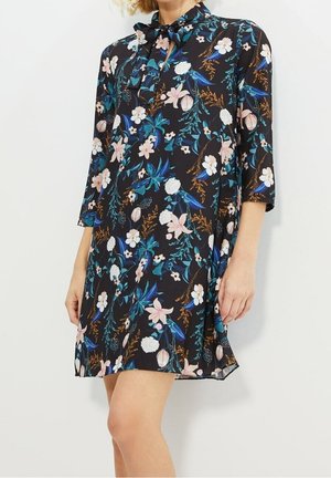 Blomsterkjole i sort stof med pink, hvide og blå blomster, trekvartærmer og bindebånd ved halsen. A-linje silhuet.