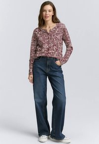 Top a maniche lunghe con motivo rosso e bianco e scollo alla henley, abbinato a jeans blu a gamba larga e sneakers bianche.