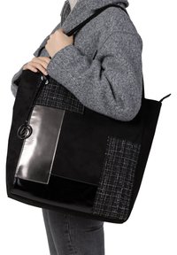 Sac fourre-tout noir avec des textures variées : daim, panneaux brillants et motif à carreaux. Il dispose d'une fermeture à glissière et d'un accent rond.