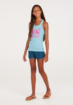 Helles blaues Tanktop mit einem pinken grafischen Design, kombiniert mit marineblauen, strukturierten Shorts. Getragen mit braunen flachen Sandalen.