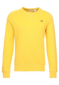 Sweat-shirt jaune en coton avec un col rond et des manches longues. Il présente un petit logo rouge sur la poitrine et des poignets côtelés.