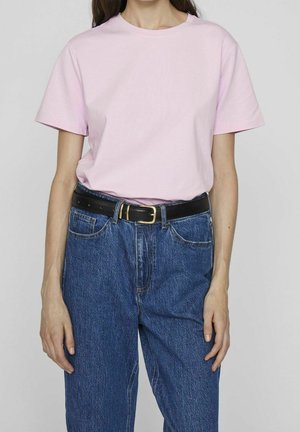 Woman wearing a light pink short-sleeve T-shirt tucked into high-waisted blue jeans with a black leather belt and gold buckle.