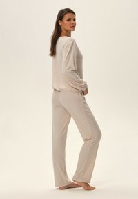 Jasnokremowy zestaw odzieży domowej, składający się z długiego rękawa topu z prążkowanej tkaniny oraz dopasowanych spodni, wykonany z miękkiego materiału o luźnym kroju.