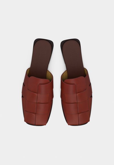 Ζευγάρι από καφέ πλεκτά δερμάτινα σανδάλια flat, με τετράγωνη μυτούλα και ανοιχτή πλάτη, σε φωτογραφία από πάνω σε λευκό φόντο.