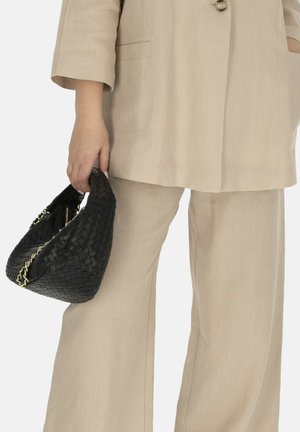 Osoba ubrana w beżowy lniany garnitur trzymająca przy boku czarną plecioną skórzaną torebkę ze złotymi łańcuszkowymi detalami.