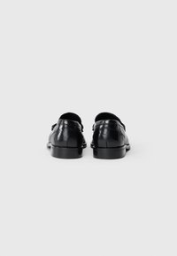 Zwarte leren schoenen met een gladde afwerking, voorzien van een lage, ronde hak en een minimalistisch ontwerp. Inclusief subtiele decoratieve hardware accenten.