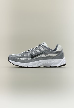 Chaussure de course Nike grise et blanche avec des panneaux en mesh, logo Swoosh noir, semelle blanche rembourrée et design à lacets vue de côté.