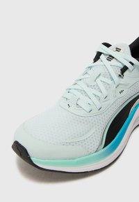 Baskets de course en maille bleu clair avec des accents noirs, surface texturée et semelle intermédiaire blanche avec un détail turquoise. Lacets et logo PUMA visibles.