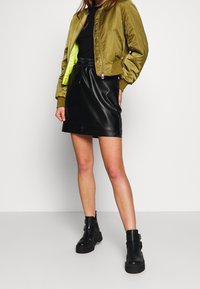 Olivgrön bomberjacka med en ljus limefärgad insida, ihopparad med en svart fusk läder minikjol och kraftiga svarta ankelskor.