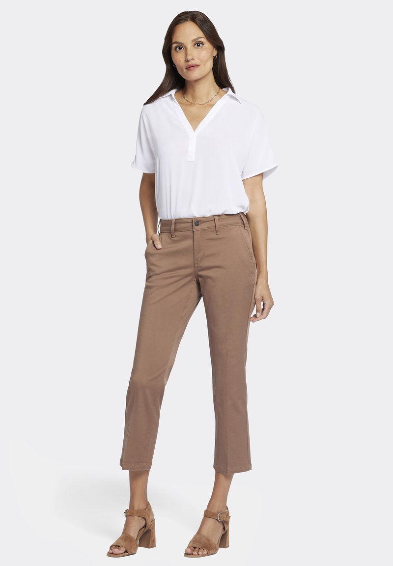 Blouse blanche à manches courtes avec un col en V, associée à un pantalon cropped slim-fit marron et des sandales à talons hauts beige. Design simple et épuré.