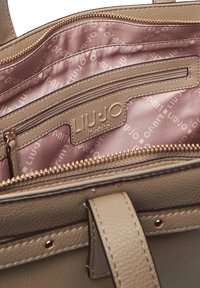 Interno di borsa beige con texture, rivestimento in satin rosa con delicato motivo a logo e una tasca con cerniera per l'organizzazione.