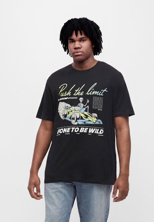 Ung mand med krøllet hår iført en sort T-shirt med grafik af en racerbilskelet og teksten "Push the limit" og "Born to be wild."