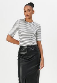 Zwart-wit gestreepte top met korte mouwen, gecombineerd met een hoge taille zwarte imitatieleren kokerrok met een split aan de voorkant.