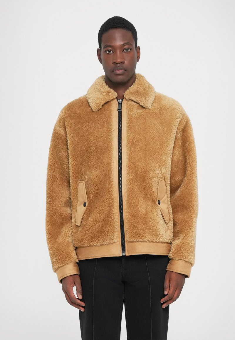 Tan faux shearling jakke med lynlås foran, spidse kraver og sidelommer. Har en blød tekstur og et afslappet fit design.