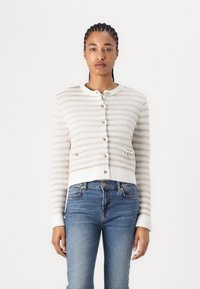 Leichter, kurzer Cardigans in Creme mit beigen Streifen, Knopfverschluss, rundem Ausschnitt und zwei kleinen Vordertaschen. Weiches, strukturiertes Strickmaterial.