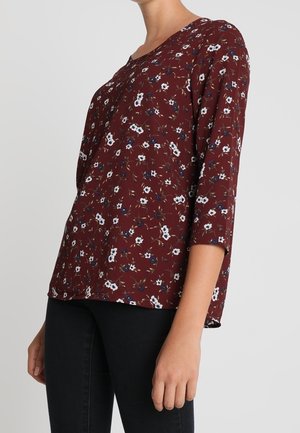 Bordowy top w kwiaty z dekoltem w serek, rękawami 3/4 oraz białymi i niebieskimi kwiatowymi wzorami. Lekki materiał, luźny krój i dół sięgający bioder.