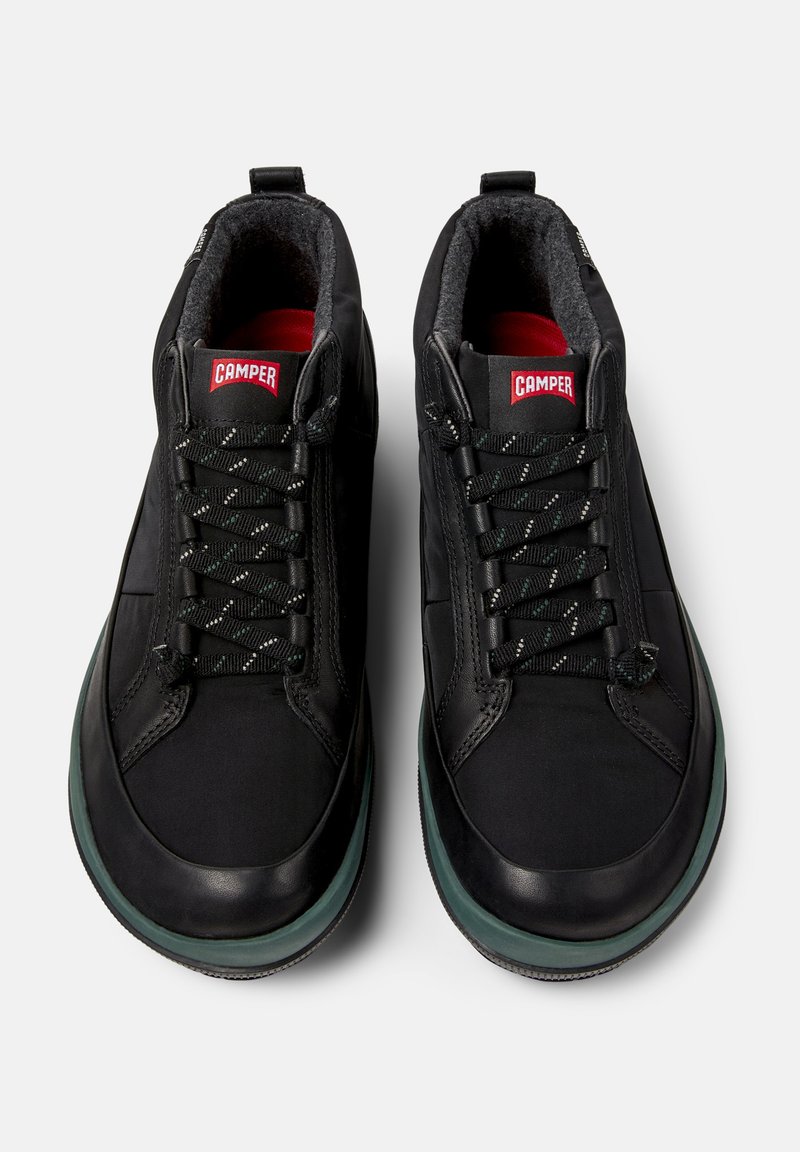 Pair of black Camper sneakers with patterned laces, padded interior, and green-accented soles, viewed from above on a white background.