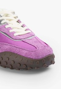 Baskets violettes avec une tige en suède et en nylon, semelle en caoutchouc brun texturé avec des motifs hexagonaux, et lacets blancs.