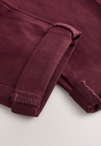 Tissu bordeaux à la texture lisse, avec des manches retroussées et des bords bruts. Vue en gros plan mettant en valeur les détails de la couture et la richesse de la couleur.