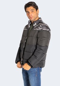Puffjacke in Schwarz und Grau Camouflage mit einem Reißverschluss vorne, hohem Kragen und gestepptem Design. Weicher Stoff mit isolierender Polsterung.