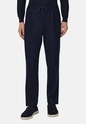 Pantalon décontracté bleu marine avec une taille élastique, fermeture à cordon de serrage et poches latérales ; il présente une texture lisse et un design minimaliste.