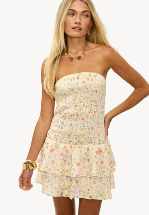 Mujer vistiendo un vestido smocked sin mangas con estampado floral multicolor y falda en capas, accesorio con pulsera dorada y collar de charms coloridos.