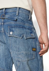 Hellblaue Denim-Jeans mit doppelten Gesäßtaschen mit Druckknopfverschluss, einem Markenetikett und einem lässigen Schnitt.