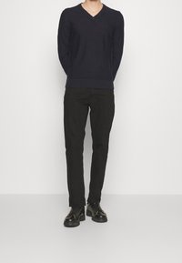 Marineblauer V-Ausschnitt-Pullover aus Strickstoff mit gerippten Bündchen, kombiniert mit schwarzen Slim-Fit-Hosen und schwarzen Schnürschuhen.