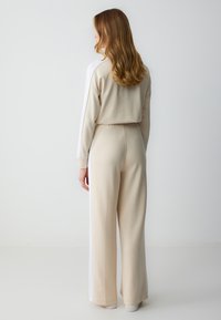 Beige trainingsoutfit met een cropped top en brede pijpen. Bevat witte zijpanelen en een zachte, gestructureerde stof. Eenvoudig, strak ontwerp.