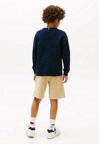 Camicia a maniche lunghe blu navy con scollatura rotonda, abbinata a pantaloni corti beige. Scarpe da ginnastica bianche con accenti colorati e calze a righe sono indossate.