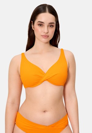 Mujer joven con cabello largo y castaño, vistiendo un bikini naranja de dos piezas con diseño de tela retorcida en la parte superior e inferior.