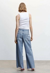 Jeans taille haute bleu clair avec jambes larges et ourlets effilochés, dotés de poches arrière, associés à un haut sans manches blanc.