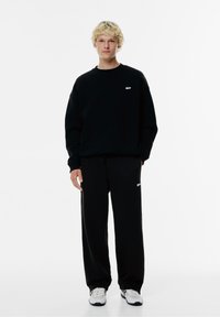 Zwart sweatshirt en sweatpants set, met een wit logo op de borst en dij, gemaakt van zachte stof, met een relaxte pasvorm en elastische boorden.