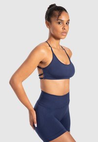 Bralette atlético de color azul marino con tiras finas y cortes laterales, combinado con pantalones cortos de compresión de tiro alto en azul marino, ambos hechos de una tela suave.