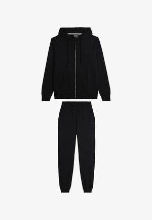 Sudadera con cremallera negra y pantalones de chándal a juego. Tejido suave, cintura con cordón, piernas ajustadas, branding mínimo visible.