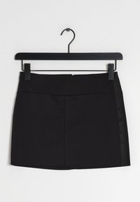 Mini-jupe noire avec une texture de tissu lisse, présentant un design simple, un panneau latéral discret et une fermeture éclair à l'arrière. Accrochée à un crochet noir.