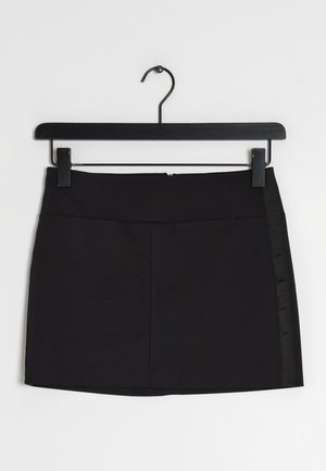 Mini-jupe noire avec une texture de tissu lisse, présentant un design simple, un panneau latéral discret et une fermeture éclair à l'arrière. Accrochée à un crochet noir.