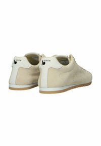 Beigen väriset mokkakengät arkikäyttöön, joissa on valkoiset kantakoristeet ja kumipohjat. Kuvattu takaa ja vinosti sivulta, kantanauhassa näkyy merkkilogot.