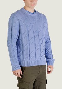 Pull tricoté bleu clair avec un motif texturé et des poignets et un ourlet côtelés, associé à un pantalon cargo vert olive.
