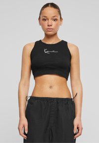 Must ümar kaelusega must ribadeta crop top valge broderi logoga. Kombineeritud vabade mustade reguleeritava paelaga pükstega.