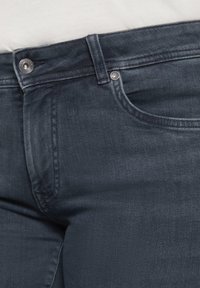 Jeans de mezclilla oscura con una textura suave, que cuentan con un cierre de botón, bolsillos frontales y sutiles detalles de costura.
