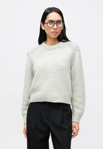 Pull gris clair en maille avec un col rond, une bordure côtelée et des détails complexes aux épaules, associé à un pantalon noir à fines rayures.