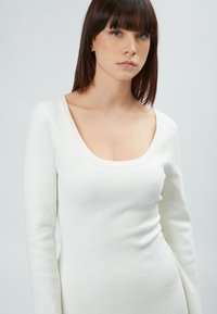 Langærmet hvid kjole med scoop-neck, tekstureret strikstof med subtile mønstre og en tætsiddende silhuet.