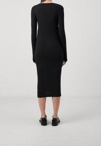 Svart, ribbad klänning med långa ärmar, figurnära silhuett och midilängd. Minimalistisk design, mjuk textur, och matchad med svarta skor.
