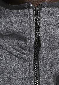 Šedá mikina na zip z měkké, texturované látky. Má černý zip s hladkým jezdcem a minimalistické designové detaily.